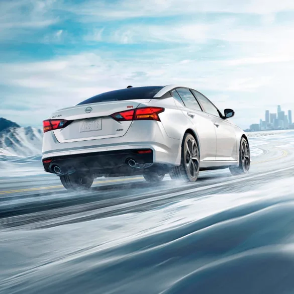 2027 Nissan Altima in white seen from behind driving in snowy landscape illustrating all-wheel drive at Reed Nissan Orlando in Orlando FL